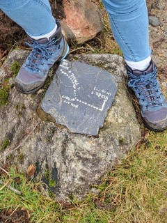 Flat stone with directions flanked by hiking boots.