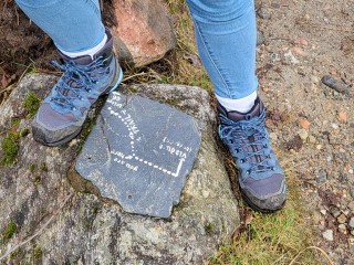 Flat stone on ground with directions written on it flanked by hiking boots