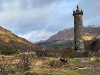 Monument with lone Scottish Highlander on top. Mountains of Scotland in the background
